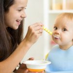 Молодая мама кормит ребенка с ложечки