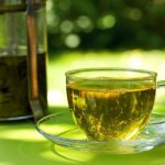 Зеленый чай в чашке и френч-прессе на зеленом фоне